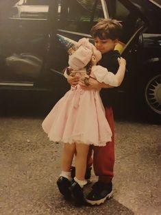 a boy and girl hugging each other in front of a car