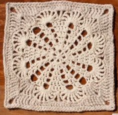 a white crocheted square with holes in the middle on a wooden table top