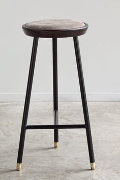 a black stool with gold legs and a white wall in the backgrounnd