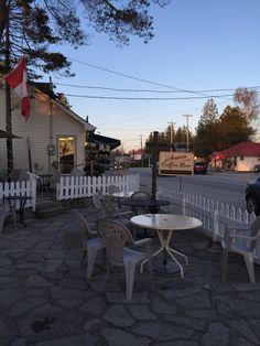 tables and chairs on the side walk near a white picket fence