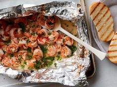 a pan filled with shrimp and garlic on top of tin foil next to slices of bread