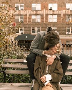 a man sitting on top of a wooden bench next to a woman who is covering her face