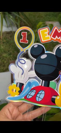 a hand holding up a mickey mouse birthday card with the number 1 on it's front