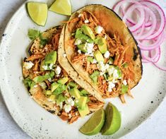 two shredded chicken tacos on a plate with sliced onions and avocado