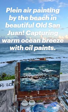 an artist's easel with paint and brushes in front of the ocean