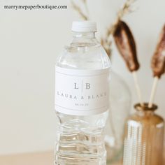 a bottle of water sitting on top of a table next to a vase with flowers