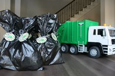 a green garbage truck parked next to a black bag filled with plastic bags on top of a hard wood floor