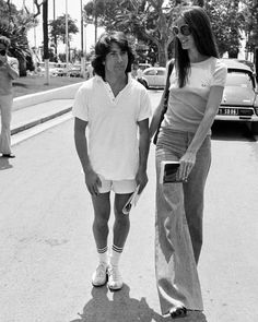 a man standing next to a woman on the side of a road while holding a skateboard