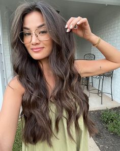 a woman with long hair and glasses posing for the camera in front of a house