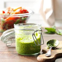 a glass jar filled with green liquid next to a wooden spoon and bowl full of salad