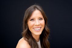 a woman with long brown hair smiling at the camera while wearing a white top and black background