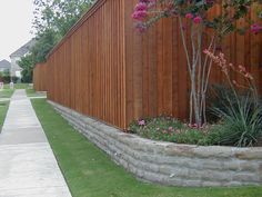 a wooden fence next to a sidewalk with flowers growing on the wall and grass in front