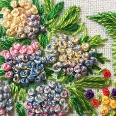 a close up of some colorful flowers on a white table cloth with green leaves and beads