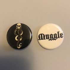 two buttons with the word muggle written in black and white, one has a snake on it