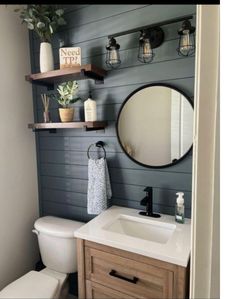 a white toilet sitting under a bathroom mirror next to a wooden sink vanity and shelf