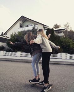 two girls are riding on skateboards in the street with their arms around each other