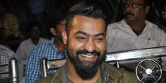 a man with a beard sitting at a table in front of other people and smiling