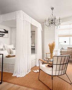 a bedroom with a bed, chandelier and two chairs in front of it