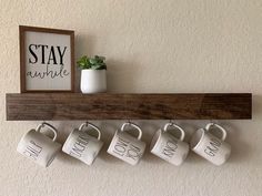 coffee mugs are hung on a shelf with the words stay awhile