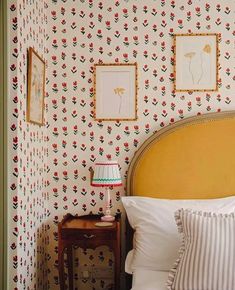 a bedroom with floral wallpaper and pictures on the wall next to a nightstand table