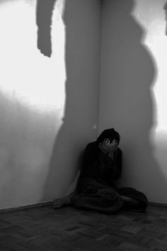 a person sitting on the floor in front of a wall with their shadow cast on it