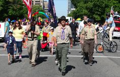 a group of people walking down a street with flags and balloons in the shape of an american flag