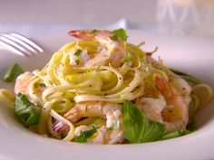 a white bowl filled with pasta and shrimp on top of a green leafy salad