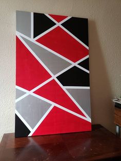 a painting on a wooden table with a white wall in the background and a black, gray, red and grey abstract design