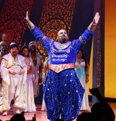 a man in blue and gold outfit standing on stage with his arms up to the sky