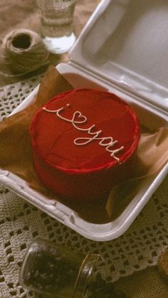 a red cake sitting in a white container on top of a table next to other items