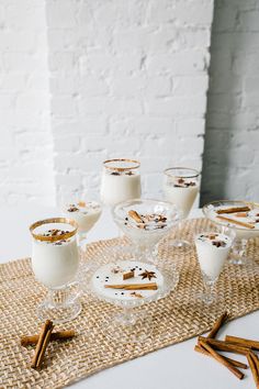 a table topped with glasses filled with desserts next to cinnamon sticks on top of a mat