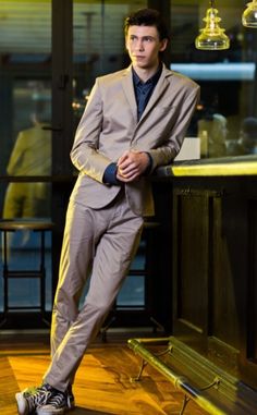 a man in a suit leaning against a bar with his foot on a bench and looking at the camera