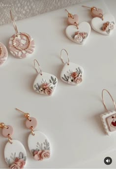 several pairs of earrings are displayed on a white surface with pink flowers and hearts in the center