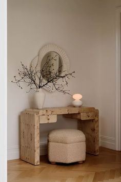 a white vase sitting on top of a wooden table next to a mirror and stool