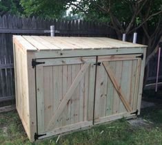 a large wooden storage box sitting in the grass next to a tree and fenced area