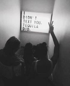 black and white photograph of three girls pointing at a sign that says i didn't text you, tequila did