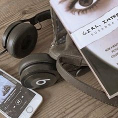 an open book, headphones and cell phone sitting on a table next to a pair of eye glasses