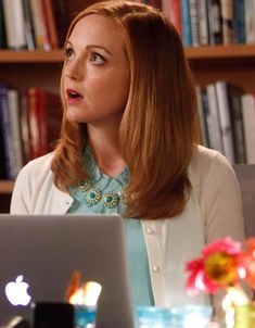 a woman sitting at a table with a laptop computer in front of her and bookshelves behind her