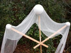 a white net and wooden stick with two balls on it in front of some bushes