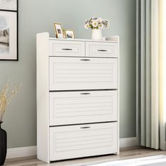 a white chest of drawers sitting next to a vase on top of a wooden floor