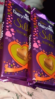 two bags of dairy milk silk chocolates on a bed with pink and yellow flowers