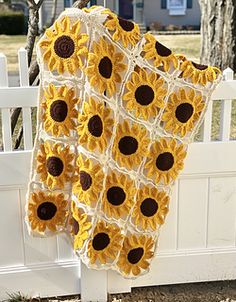 a sunflower blanket hanging on a white fence