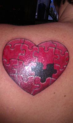 a heart shaped puzzle piece tattoo on the back of a woman's shoulder,