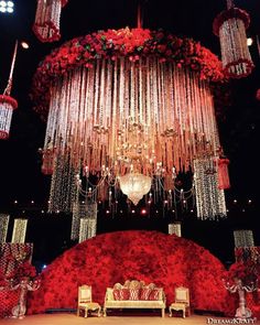 a chandelier hanging from the ceiling over a stage with red flowers on it