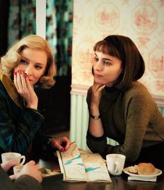 two women sitting at a table with coffee cups