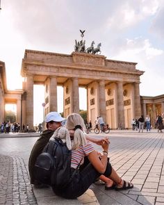 a man and woman sitting on the ground in front of a building with an arch