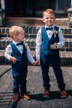 two young boys dressed in blue vests and bow ties holding hands with each other