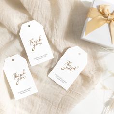 three thank you gift tags sitting on top of a white cloth next to a box