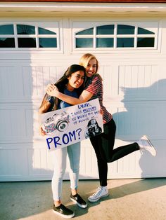 two young women are hugging each other in front of a garage door holding a sign that says prom