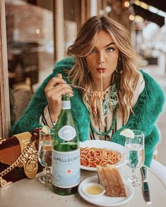 a woman sitting at a table with food in front of her and drinking from a bottle